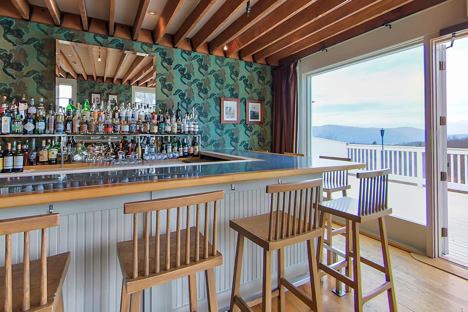 Bar at The Garrison in Garrison, NY, with wood stools, a beamed ceiling and doors open to the deck
